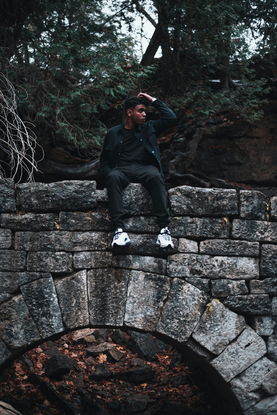 man in black jacket and black pants sitting on concrete wall