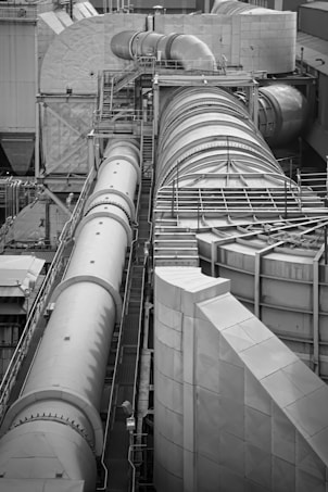 A complex industrial structure featuring large cylindrical pipes and ducts connected to various platforms and support structures. The environment suggests a manufacturing or processing plant, with metallic surfaces and geometric patterns visible.