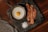 A fried egg is served in a small cast-iron skillet alongside three crispy strips of bacon. Coarse salt is scattered on a dark slate serving board placed on a wooden table. A textured gray cloth napkin is partially visible in the corner.
