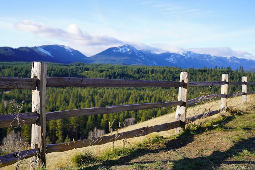 une clôture en bois sur une colline herbeuse avec des montagnes en arrière-plan