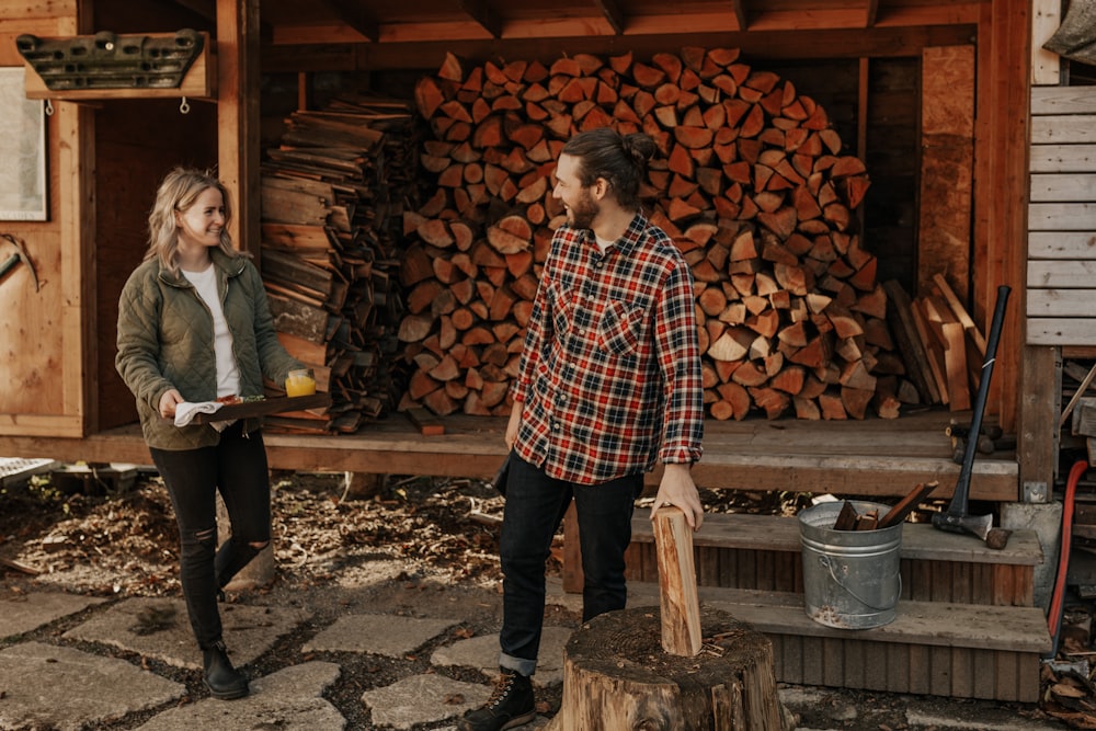 man in red and black checkered dress shirt and black pants standing beside brown wood logs