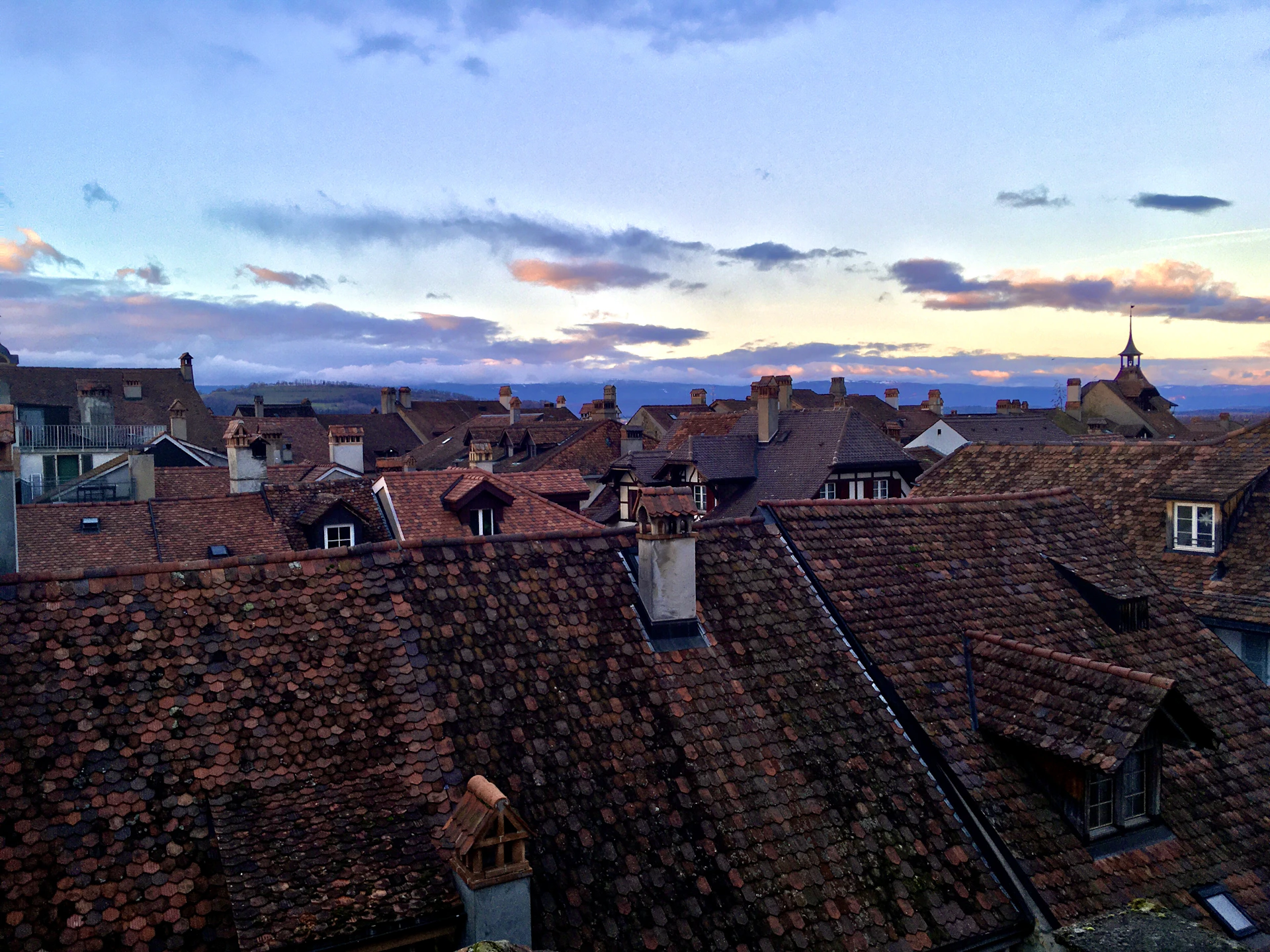 A scenic panorama of a vibrant town with terracotta rooftops under a glowing sunset sky.