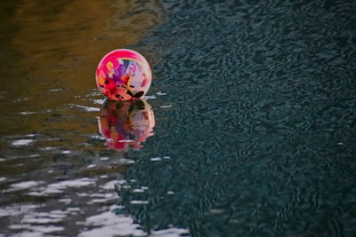 A colorful inflatable ball with cartoon characters partially submerged and floating on rippling water.