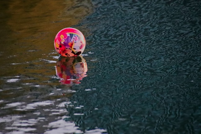 A colorful inflatable ball with cartoon characters partially submerged and floating on rippling water.