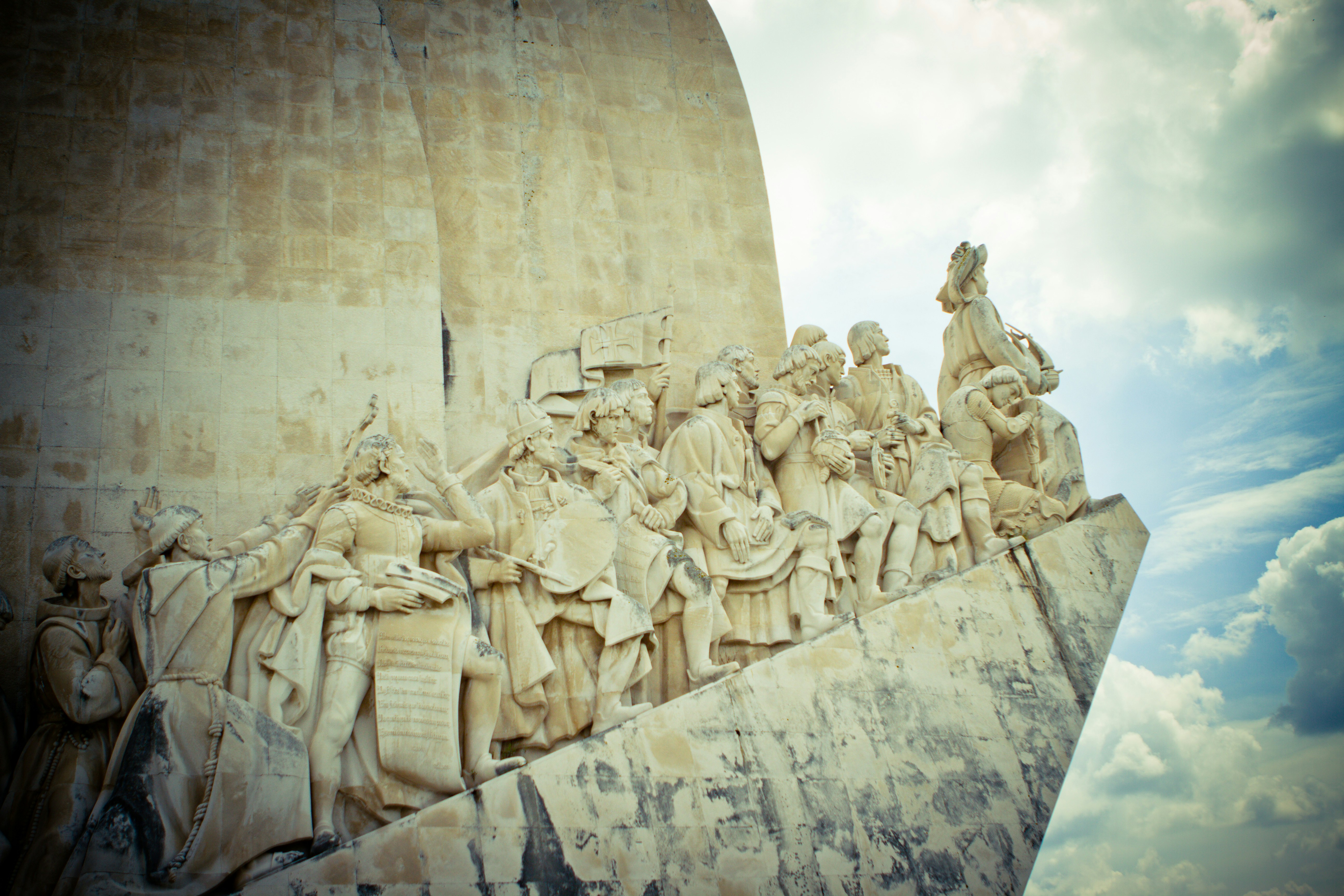 people sitting on bench statue under white clouds during daytime