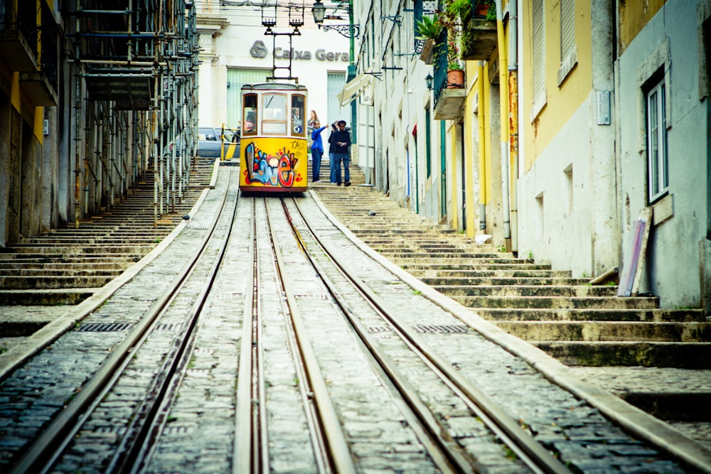 yellow and white train in between of white concrete buildings during daytime