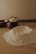 A wooden kitchen table is covered with baking ingredients including a mound of flour, some butter cubes in a black cup, an egg, and a wooden bowl. The setting has a warm, soft lighting that creates a cozy and rustic atmosphere.