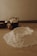 A wooden kitchen table is covered with baking ingredients including a mound of flour, some butter cubes in a black cup, an egg, and a wooden bowl. The setting has a warm, soft lighting that creates a cozy and rustic atmosphere.