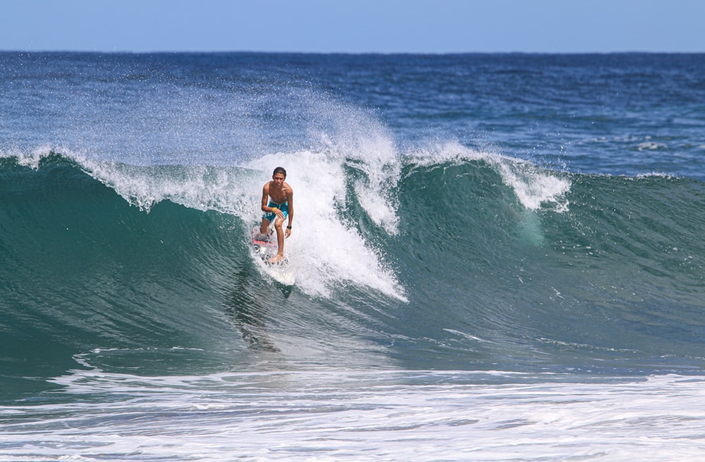 hombre en pantalones cortos azules surfeando en las olas del mar durante el día