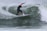 A surfer skillfully rides a wave, executing a dynamic turn on a surfboard. The wave is curling around the surfer, creating a dramatic splash. The person is wearing a wetsuit, and the ocean appears agitated and lively.