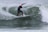 A surfer skillfully rides a wave, executing a dynamic turn on a surfboard. The wave is curling around the surfer, creating a dramatic splash. The person is wearing a wetsuit, and the ocean appears agitated and lively.
