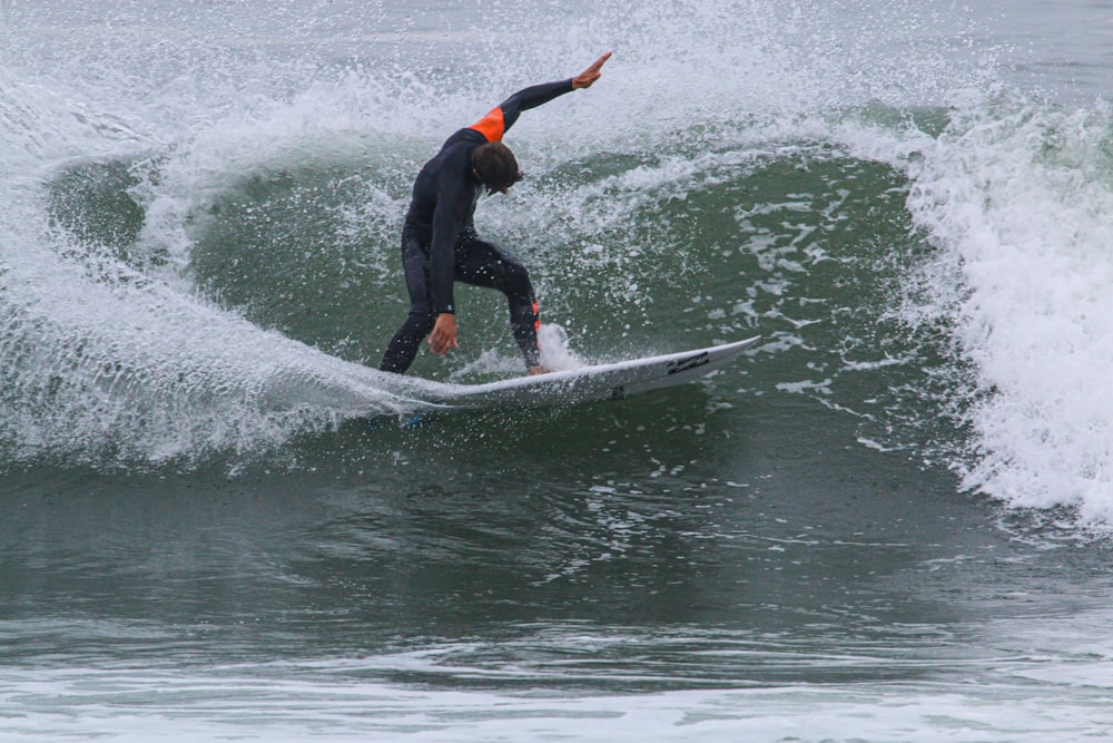 hombre con traje de neopreno negro surfeando en el agua durante el día