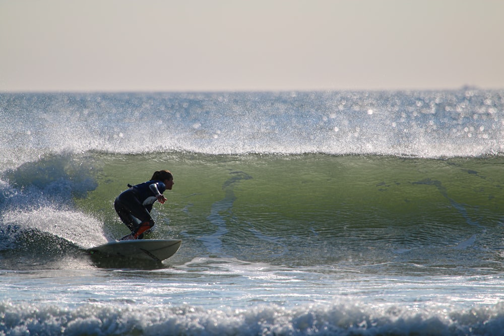 man in black wet suit riding on blue surfboard on sea during daytime