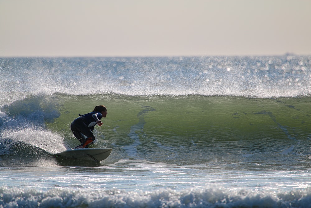 homem em traje de mergulho preto que monta na prancha de surf azul no mar durante o dia