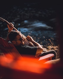 man in black tank top and blue shorts sitting on orange chair
