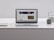 A laptop with an open webpage sits on a white marble table, surrounded by a notebook, a cup, and a kettle. The webpage shows a science-related article with images and text.