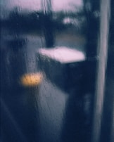 Soft focus on a window with raindrops falling slowly, with amber light glowing inside.