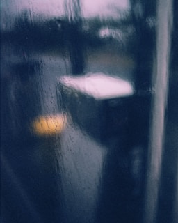 Soft focus on a window with raindrops falling slowly, with amber light glowing inside.