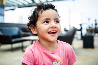 A joyful toddler wearing a pink unicorn-themed outfit, smiling in a bright, colorful room.