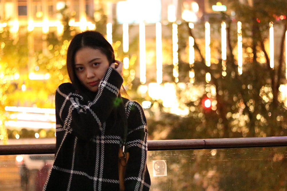 woman in black and white plaid coat standing near railings during night time