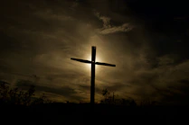 A warm sunrise over a peaceful countryside with a subtle cross silhouette.