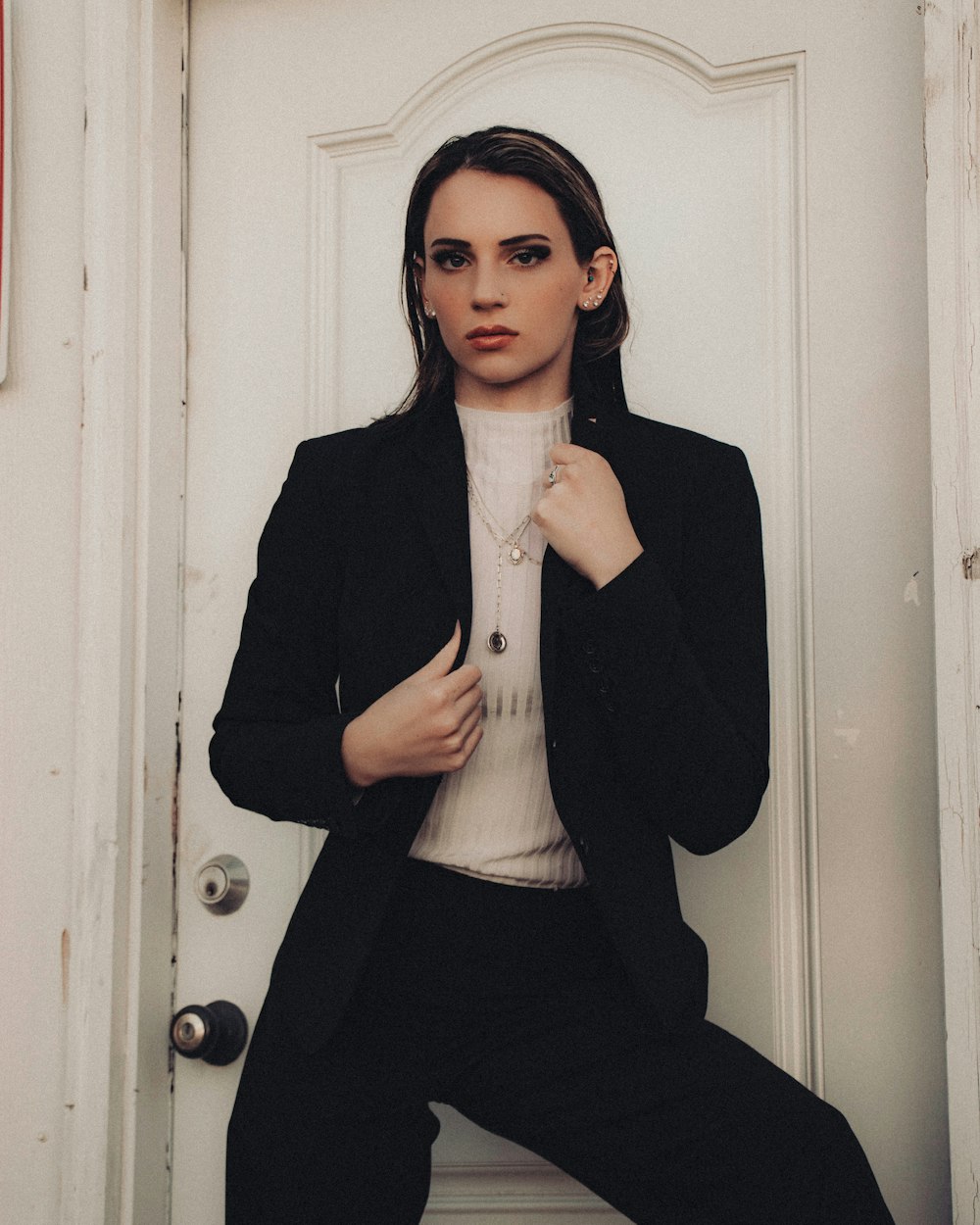 woman in black blazer and white shirt standing beside white wooden door