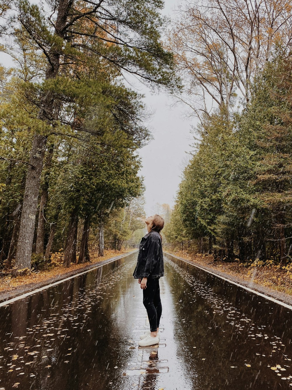 woman in black coat walking on pathway between trees during daytime