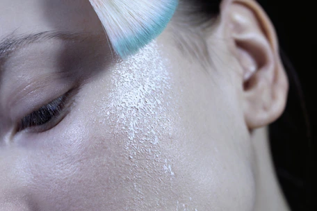 Close-up of a hand applying shimmering highlighter on cheekbones with a soft brush.