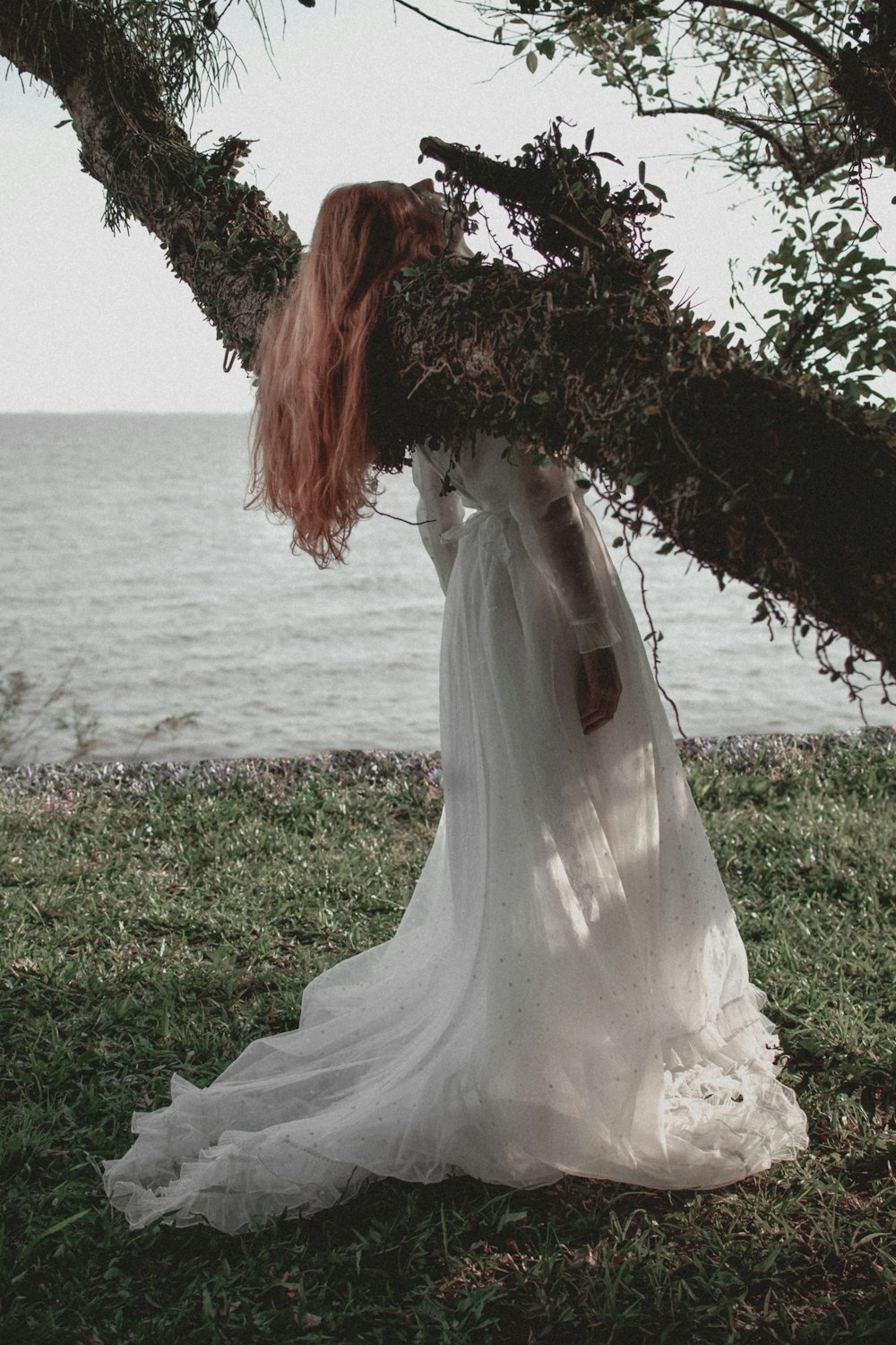 donna in abito da sposa bianco in piedi sul campo di erba verde vicino allo specchio d'acqua durante il giorno