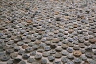A large collection of broken ceramic plates and bowls spread out on a surface, featuring intricate blue patterns on a predominantly white background. The ceramics appear to be deliberately arranged in an artistic manner.