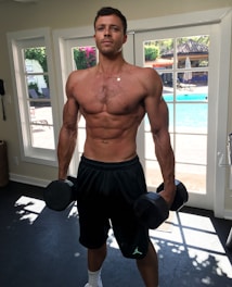 topless man in black shorts holding black dumbbell