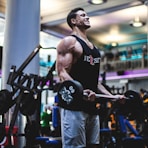 man in black tank top and blue pants holding black exercise equipment