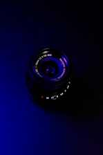 Close-up of a professional camera lens emitting a subtle blue glow over a dark background.