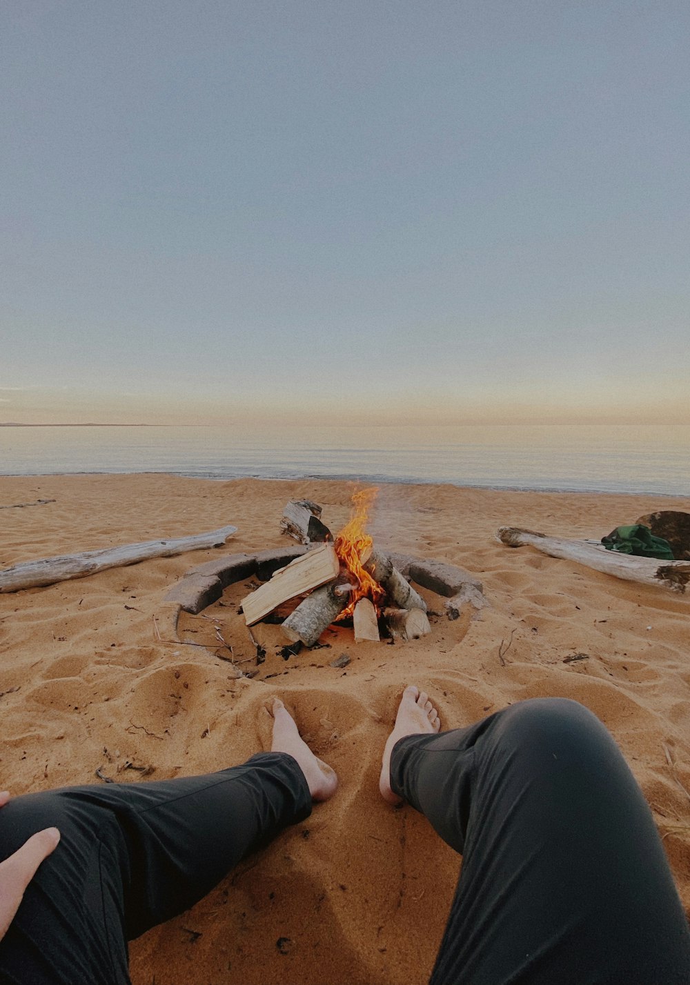 two people sitting on a beach near a fire pit