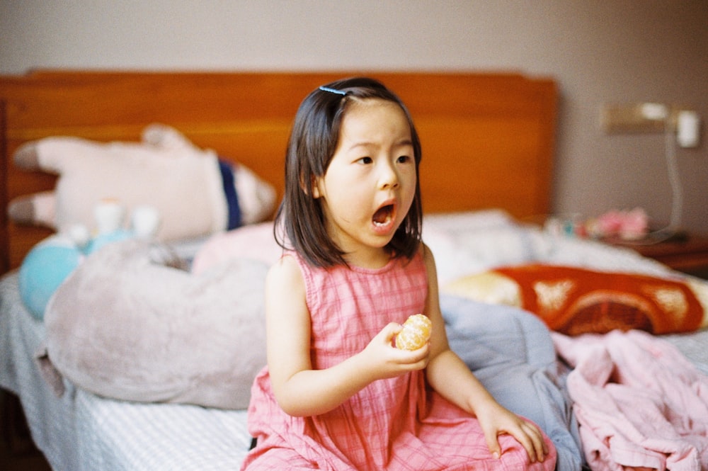 girl in pink sleeveless dress sitting on bed