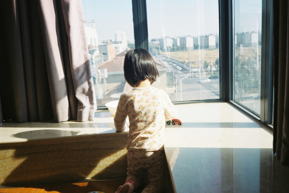 girl in white and pink floral long sleeve dress standing beside glass window during daytime