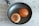 A frying pan contains two burger buns, one toasted and the other plain with sesame seeds. The pan sits on a wooden surface.