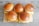 Five hamburgers with sesame seed-topped buns are arranged on a wooden serving board. The burgers include cheese and a visible beef patty, and they are placed neatly on a textured surface with a grayish tone.