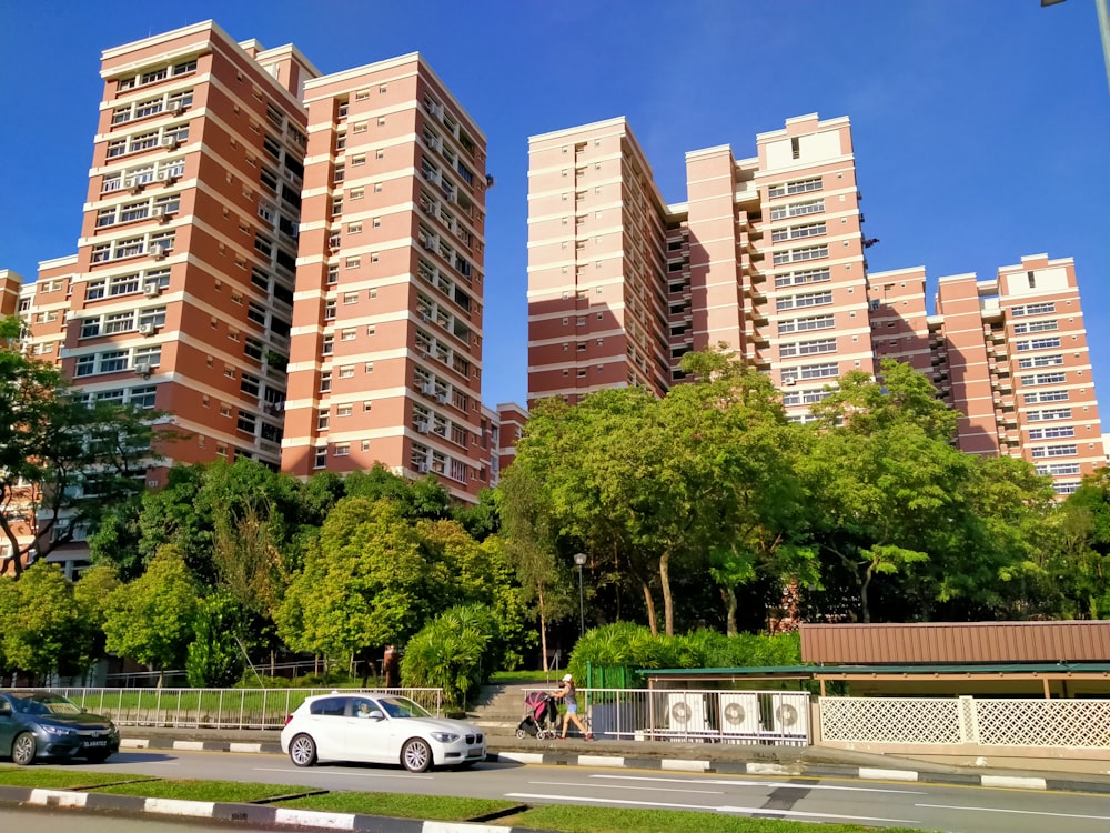 white sedan parked on gray asphalt road near green trees and brown high rise building during