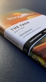 A close-up view of a notebook titled 'The Farm Edition Storyboard'. The cover features colorful abstract designs, and the notebook is thread-bound with a visible spine. The words are printed clearly, and the notebook is resting on a textured, dark surface.