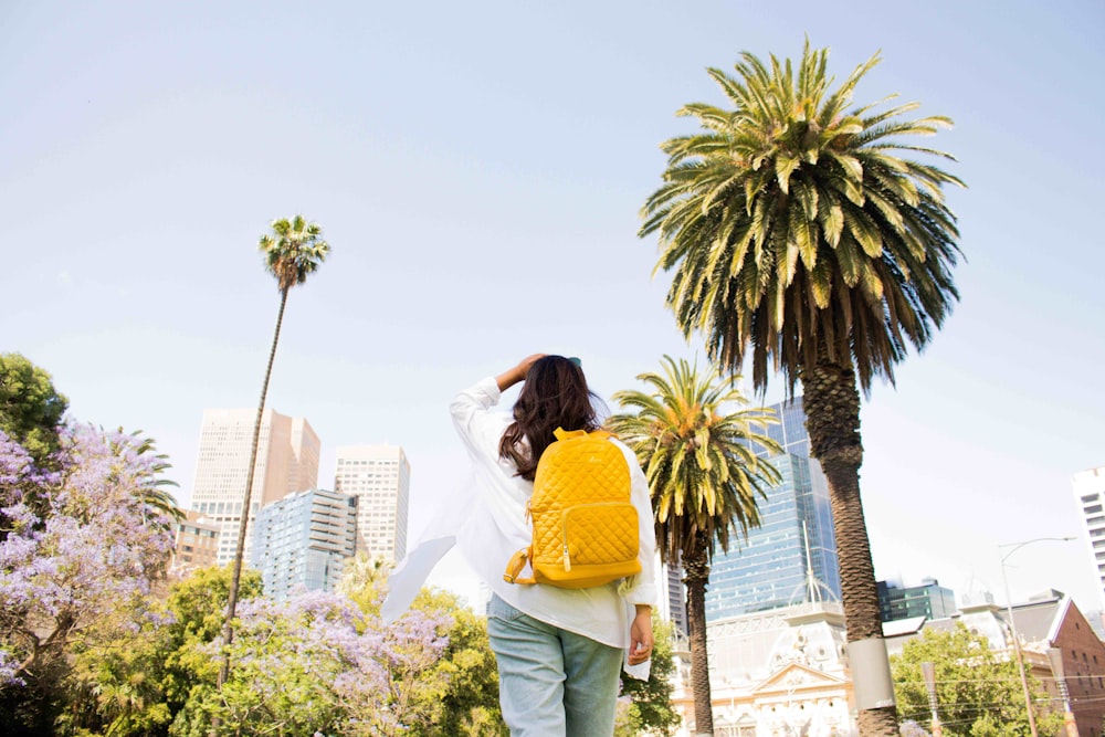 Femme en chemise jaune et pantalon blanc debout près d’un palmier pendant la journée