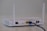 A white wireless router with two antennas is placed on a flat surface. The back of the router is visible, showing various ports including a yellow Ethernet port with a blue cable connected, power input, and a power switch.