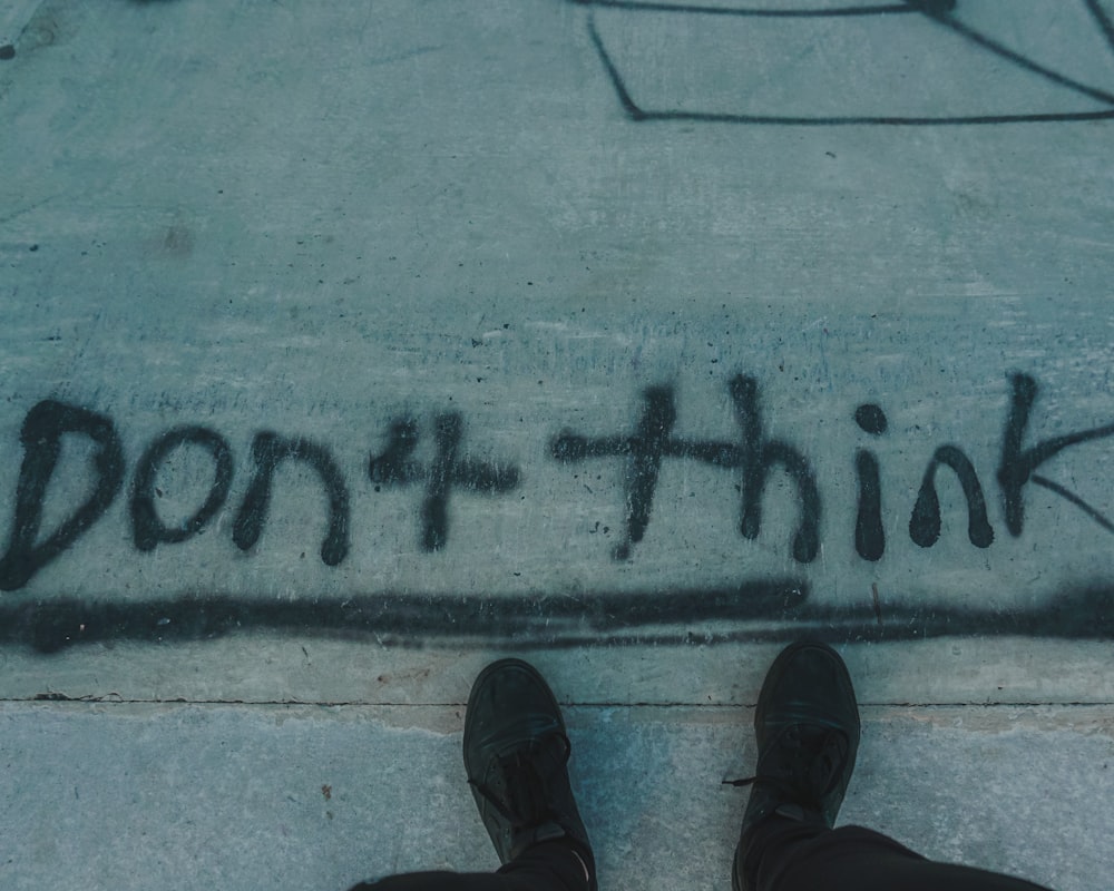 person in black leather shoes standing on gray concrete floor