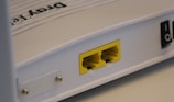 A close-up view of a white rectangular electronic device featuring two yellow Ethernet ports labeled P1 and P2. It has a smooth surface with some text that appears embossed on the top.