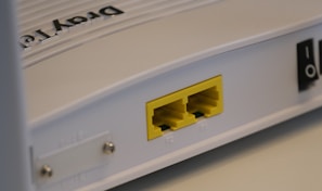 A close-up view of a white rectangular electronic device featuring two yellow Ethernet ports labeled P1 and P2. It has a smooth surface with some text that appears embossed on the top.