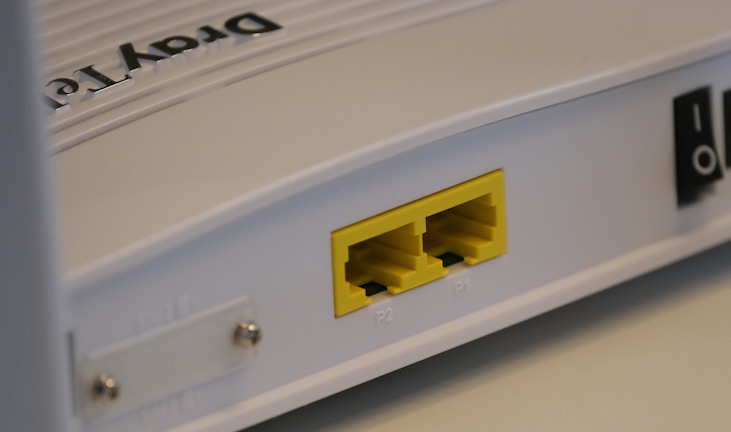 A close-up view of a white rectangular electronic device featuring two yellow Ethernet ports labeled P1 and P2. It has a smooth surface with some text that appears embossed on the top.