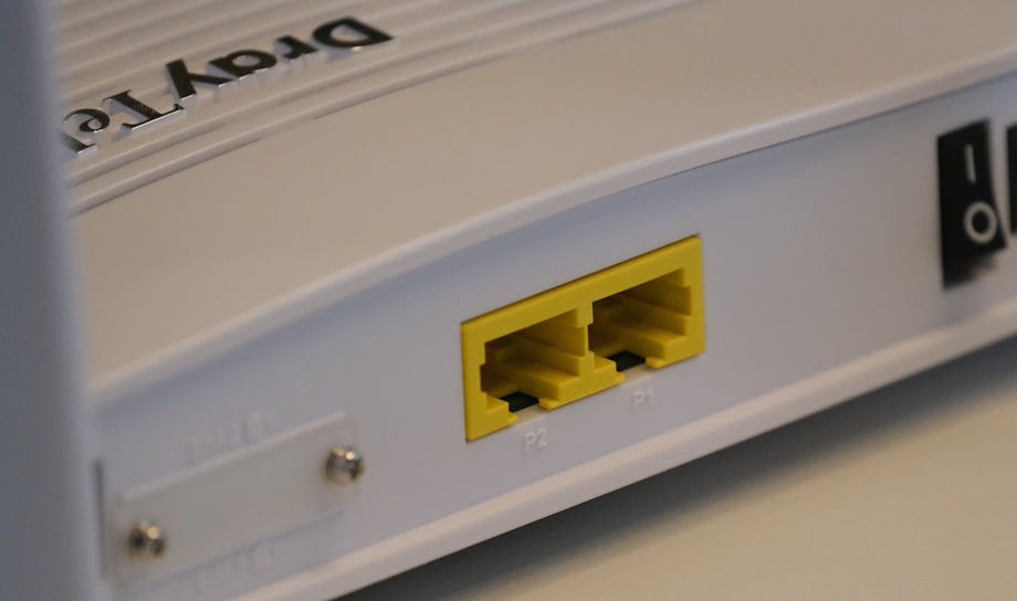 A close-up view of a white rectangular electronic device featuring two yellow Ethernet ports labeled P1 and P2. It has a smooth surface with some text that appears embossed on the top.