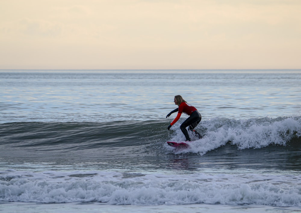 man in red shirt surfing on sea waves during daytime