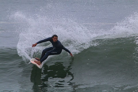 A surfer skillfully rides a large wave, maintaining balance and control. The spray of water forms a dramatic arc behind him, highlighting the speed and movement involved in the surfing maneuver. Dressed in a wetsuit, the surfer exhibits focus and agility in the challenging ocean environment.