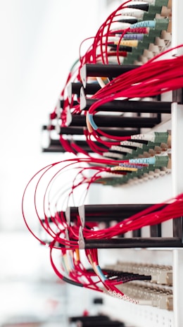 A collection of red cables is neatly organized and connected to various ports on a network rack. The cables are looped orderly, suggesting a structured setup, and the overall scene has a high-tech, organized appearance.